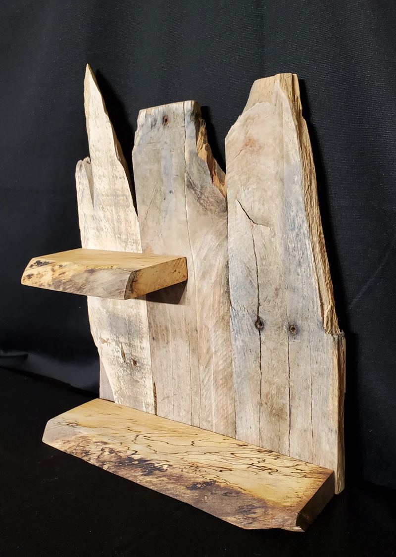 A wall shelf made of weathered grey planks with two live-edge shelves.