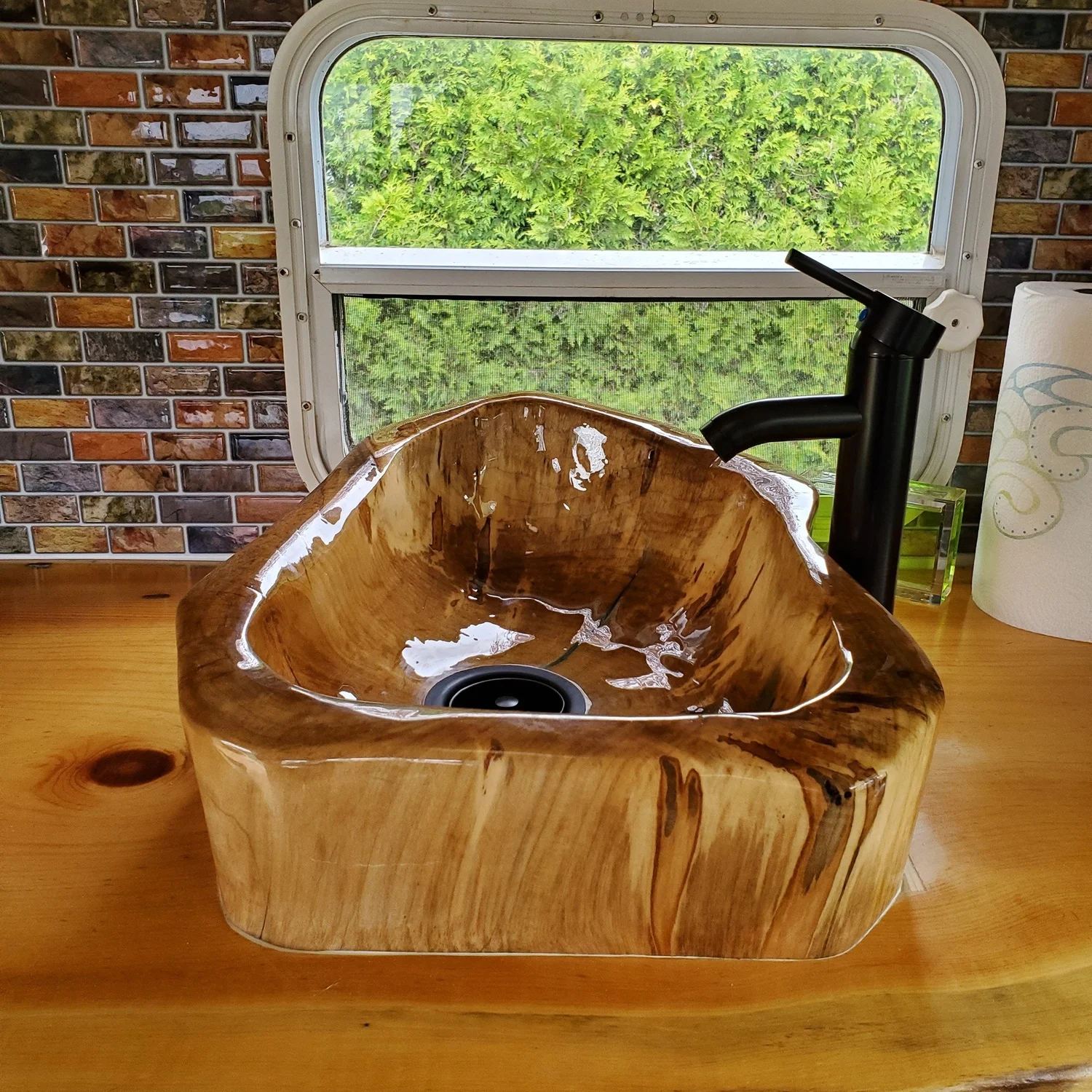 A glossy vessel sink hollowed from one piece of maple, sitting on a pine counter under a black faucet.